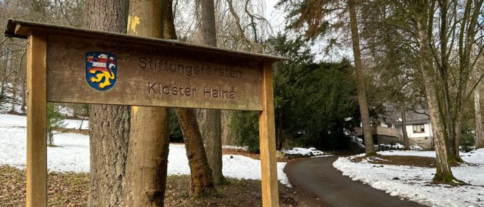 Holzschild Stiftungsforsten Kloster Haina an einem verschneiten Waldweg.